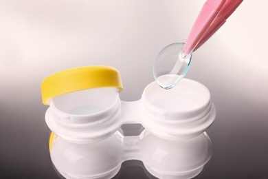 Taking contact lens from case on grey background, closeup