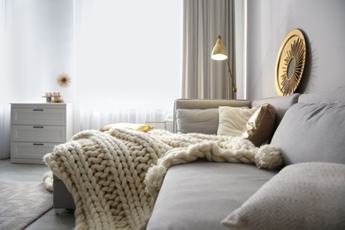 Comfortable sofa with warm knitted blanket in living room. Interior design