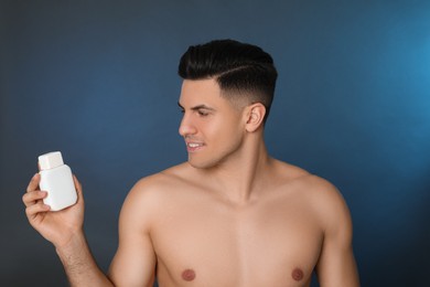 Handsome man holding post shave lotion on blue background