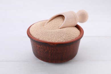 Photo of Bowl and scoop with active dry yeast on white wooden table