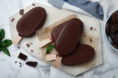 Delicious glazed ice cream bars with mint and chocolate on white marble table, flat lay