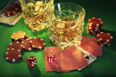 Casino chips, dice, playing cards and glasses of whiskey on green table
