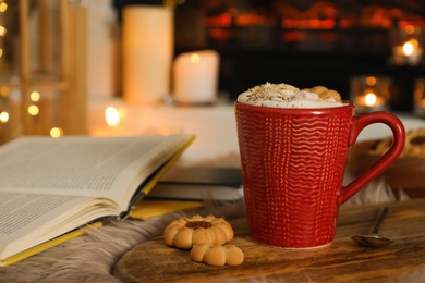 Cup of cocoa, books and cookies near fireplace indoors