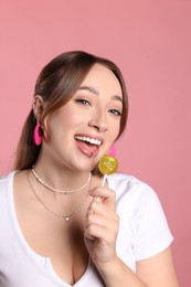 Young woman with lip and ear piercings holding lollipop on pink background