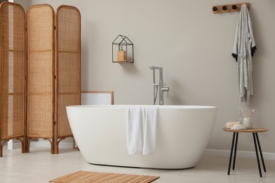 Modern ceramic bathtub and folding screen near white wall in room