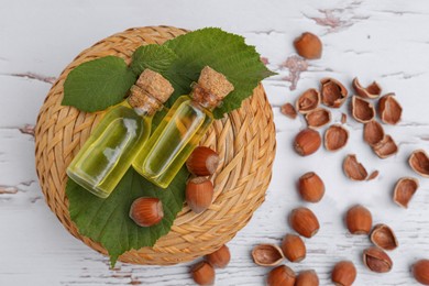 Bottles of hazelnut essential oil and nuts on wooden table, flat lay