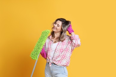 Beautiful young woman with mop singing on orange background