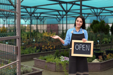 Photo of Female business owner holding OPEN sign in greenhouse. Space for text