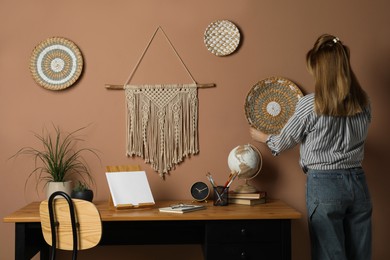 Photo of Woman hanging wicker wall decor near stylish macrame over workplace, back view