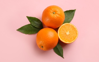 Fresh ripe oranges with green leaves on pink background, flat lay