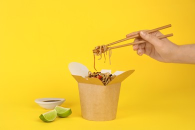 Woman eating seafood wok noodles with chopsticks from box on yellow background, closeup