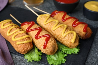 Delicious deep fried corn dogs with lettuce and sauces on grey table, closeup