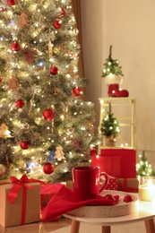 Red cup on white table in room with Christmas tree. Festive interior design