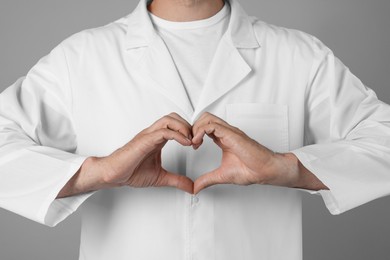 Doctor making heart with hands on grey background, closeup