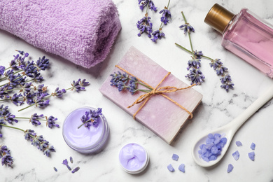 Cosmetic products and lavender flowers on white marble table, flat lay