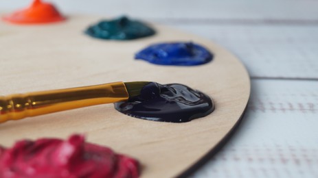 Photo of Artist's palette with samples of colorful paints and brush on white wooden table, closeup