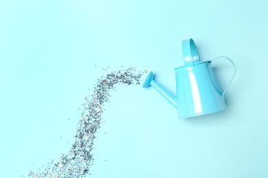 Watering can with silver glitter confetti imitating water  flow on cyan background, flat lay
