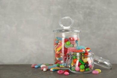Jars with different delicious candies on grey table, space for text