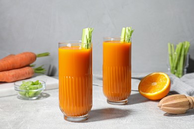Photo of Glasses of tasty carrot juice with celery sticks on light grey table