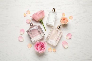 Flat lay composition with different perfume bottles and roses on white wooden background
