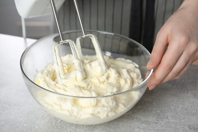 Woman whipping white cream with mixer at light grey table, closeup
