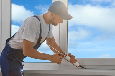 Worker sealing plastic window with caulk indoors. Installation process