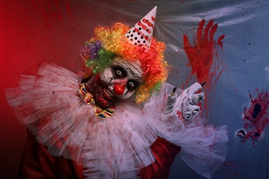 Terrifying clown near bloodstained plastic film. Halloween party costume