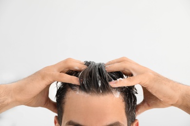 Man applying shampoo onto his hair against light background, closeup. Space for text