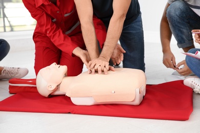 Group of people with instructor practicing CPR on mannequin at first aid class indoors, closeup