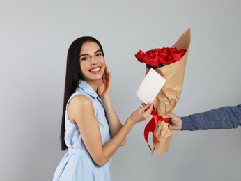 Happy woman receiving red tulip bouquet and greeting card from man on light grey background. 8th of March celebration
