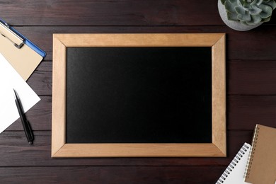 Clean small chalkboard, plant and stationery on wooden table, flat lay