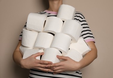 Woman with heap of toilet paper rolls on beige background, closeup