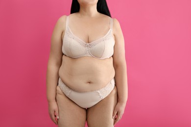 Overweight woman in beige underwear on pink background, closeup. Plus-size model