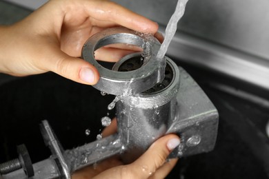 Photo of Woman washing manual meat grinder under tap water in kitchen sink indoors, closeup