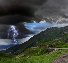 Dark cloudy sky with lightning striking ground. Thunderstorm in mountains