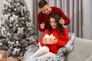 Young man presenting Christmas gift to his girlfriend at home