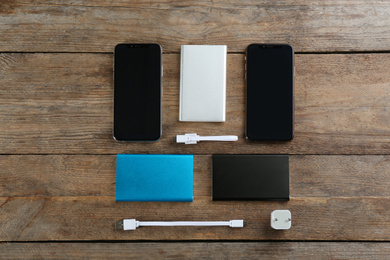 Flat lay composition with mobile phones and portable chargers on wooden background