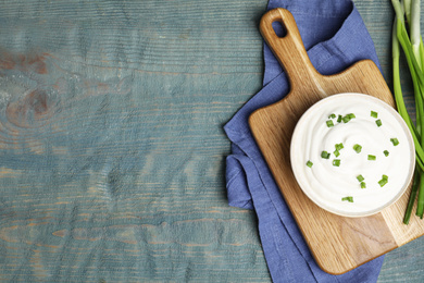 Fresh sour cream with onion on light blue wooden table, flat lay. Space for text