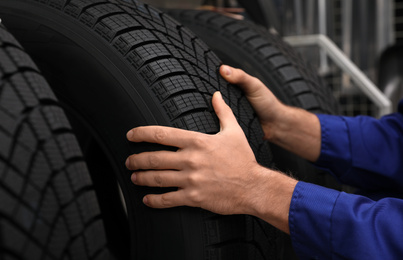 Male mechanic with car tire in auto store, closeup