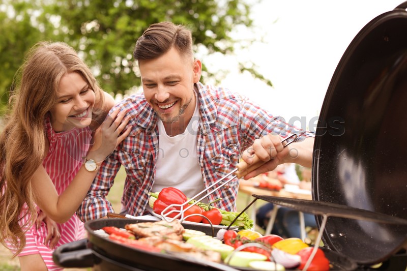 Photo of Young couple having barbecue with modern grill outdoors
