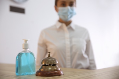 Receptionist at countertop in hotel, focus on dispenser bottle with antiseptic gel and service bell. Space for text