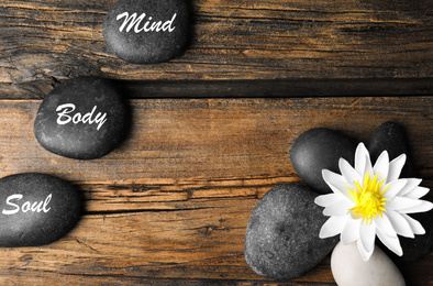 Flat lay composition of lotus flower and stones with words Mind, Body, Soul on wooden background, space for text. Zen lifestyle