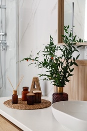 Vase with beautiful branches, candles and air reed freshener near vessel sink in bathroom. Interior design