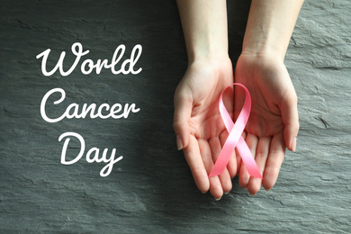 Woman holding pink ribbon on grey stone background, top view. World Cancer Day