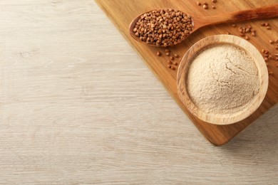 Bowl of buckwheat flour and spoon with grains on white wooden table, flat lay. Space for text