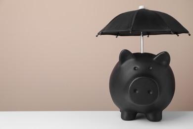 Small umbrella and piggy bank on white table. Space for text