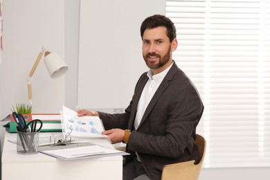 Photo of Businessman putting document into punched pocket at white table in office