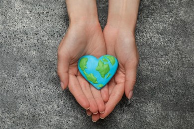 Happy Earth Day. Woman with heart shaped plasticine planet at grey table, top view