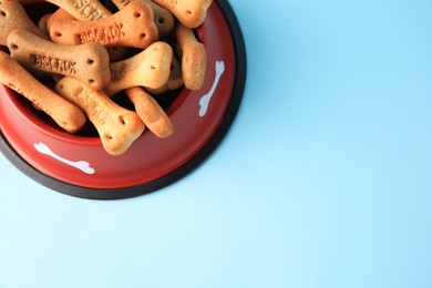 Photo of Bone shaped dog cookies in feeding bowl on light blue background, above view. Space for text
