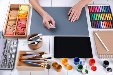Artist drawing with chalk pastel on grey paper at white wooden table, above view